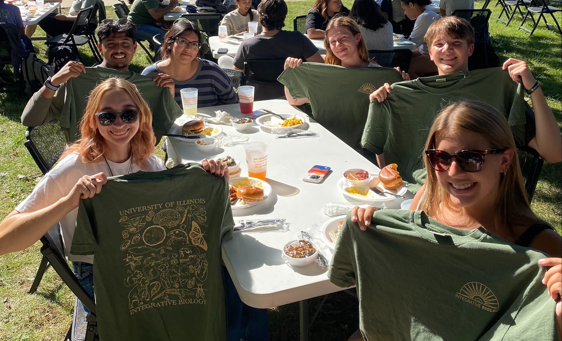 students holding up shirts at a table outside