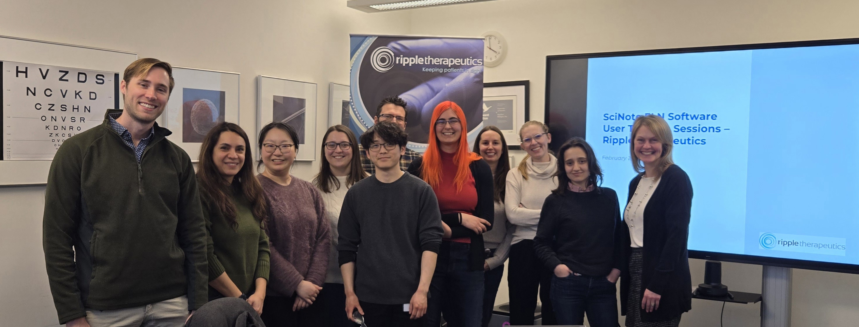 a group of people standing and smiling in front of a sign and digital screen
