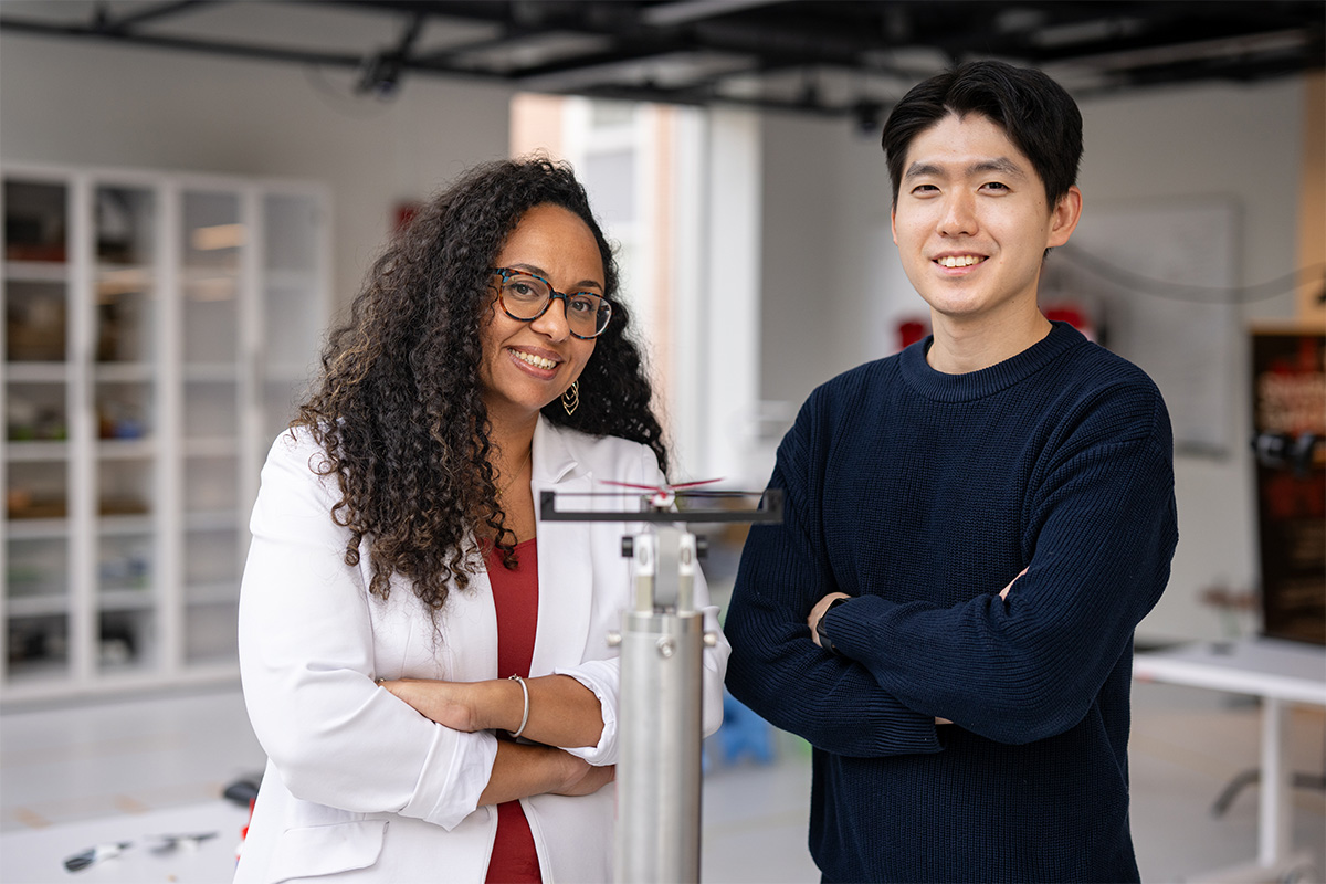 A man in a blue sweater and a woman in a lab coat crossing their arms and smiling at the camera.