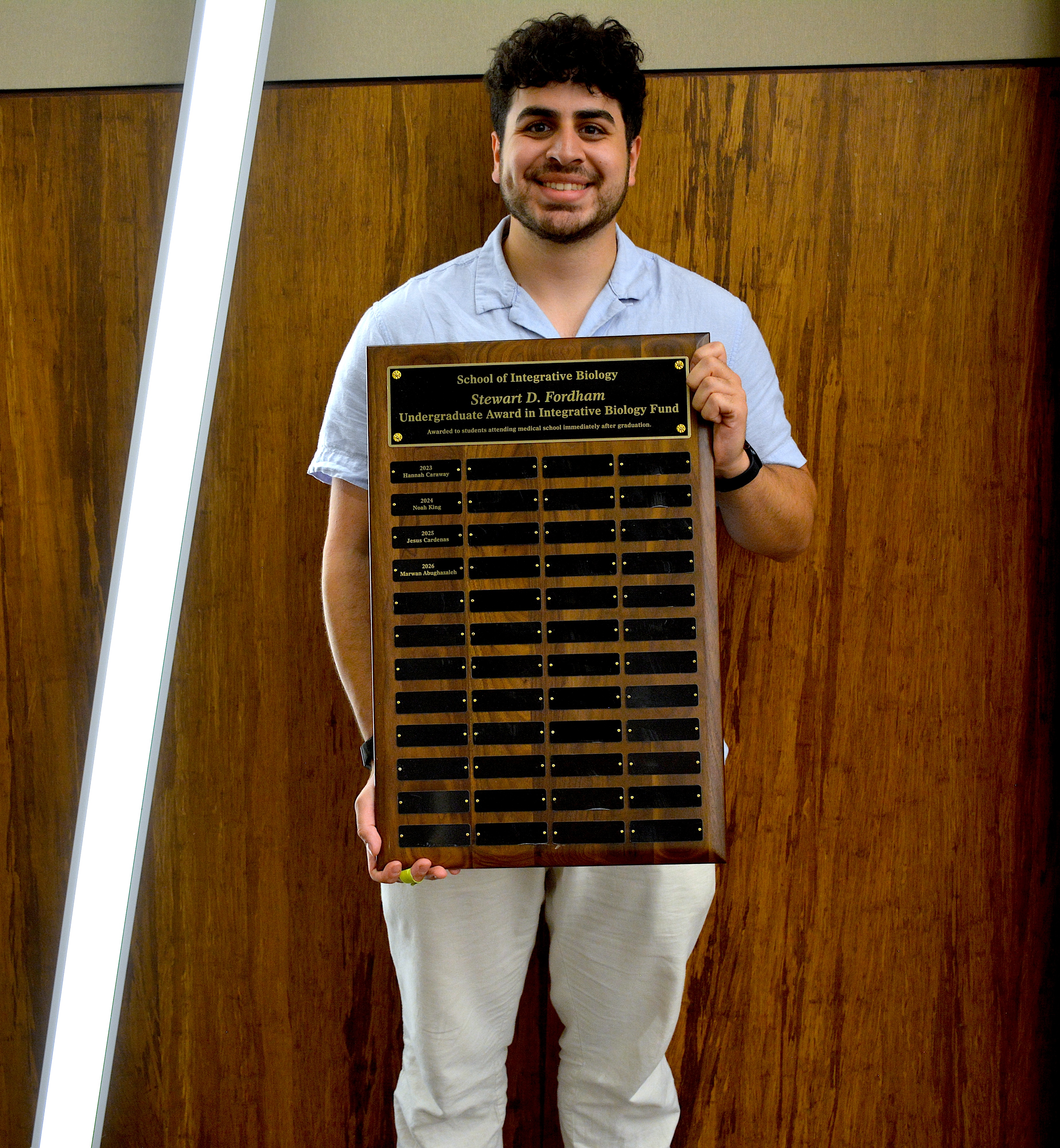 A smiling student holding a plaque