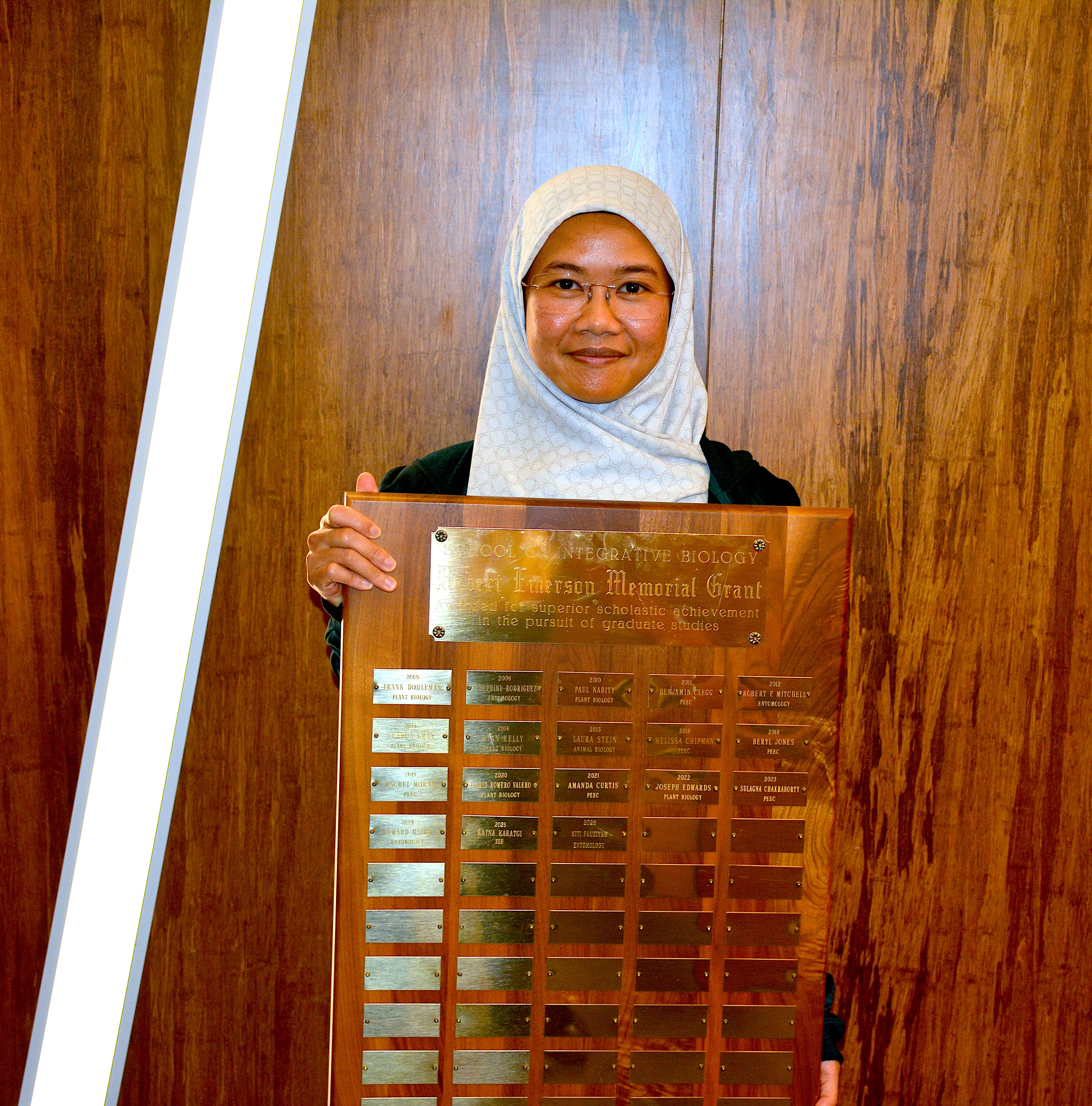 A smiling student holding a plaque