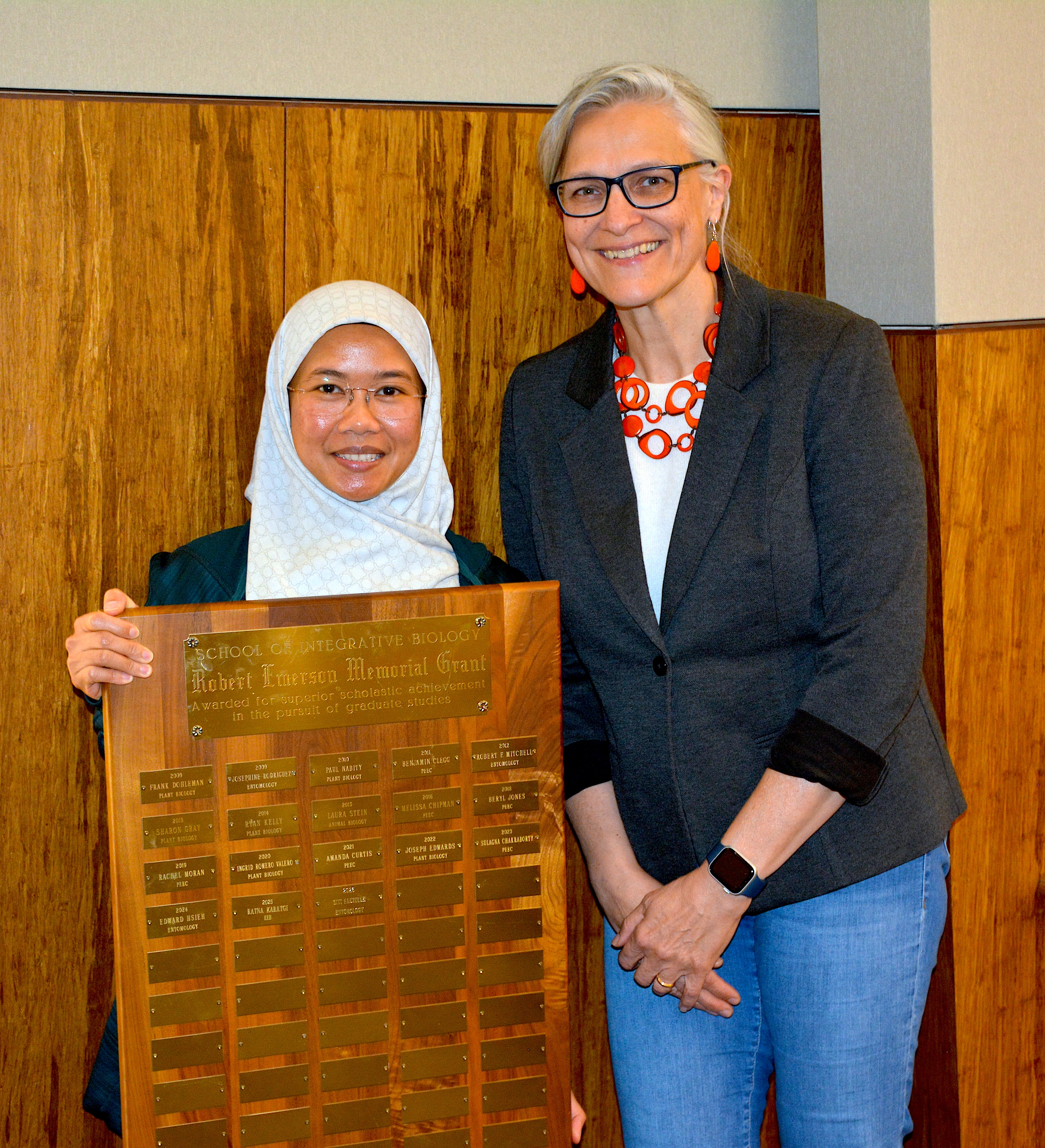 A student holding a plaque standing next to their mentor