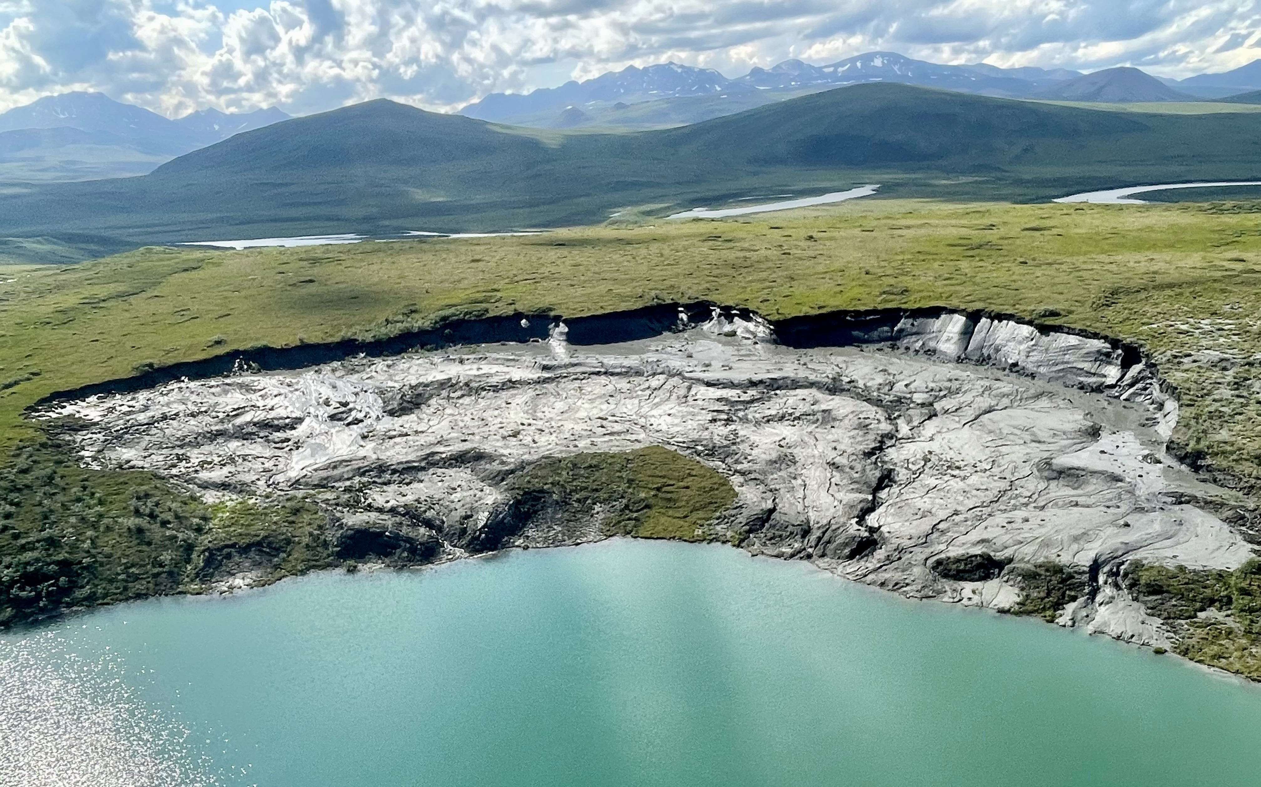 Mountains in the background, green flatlands in the middle, stone and water in the foreground