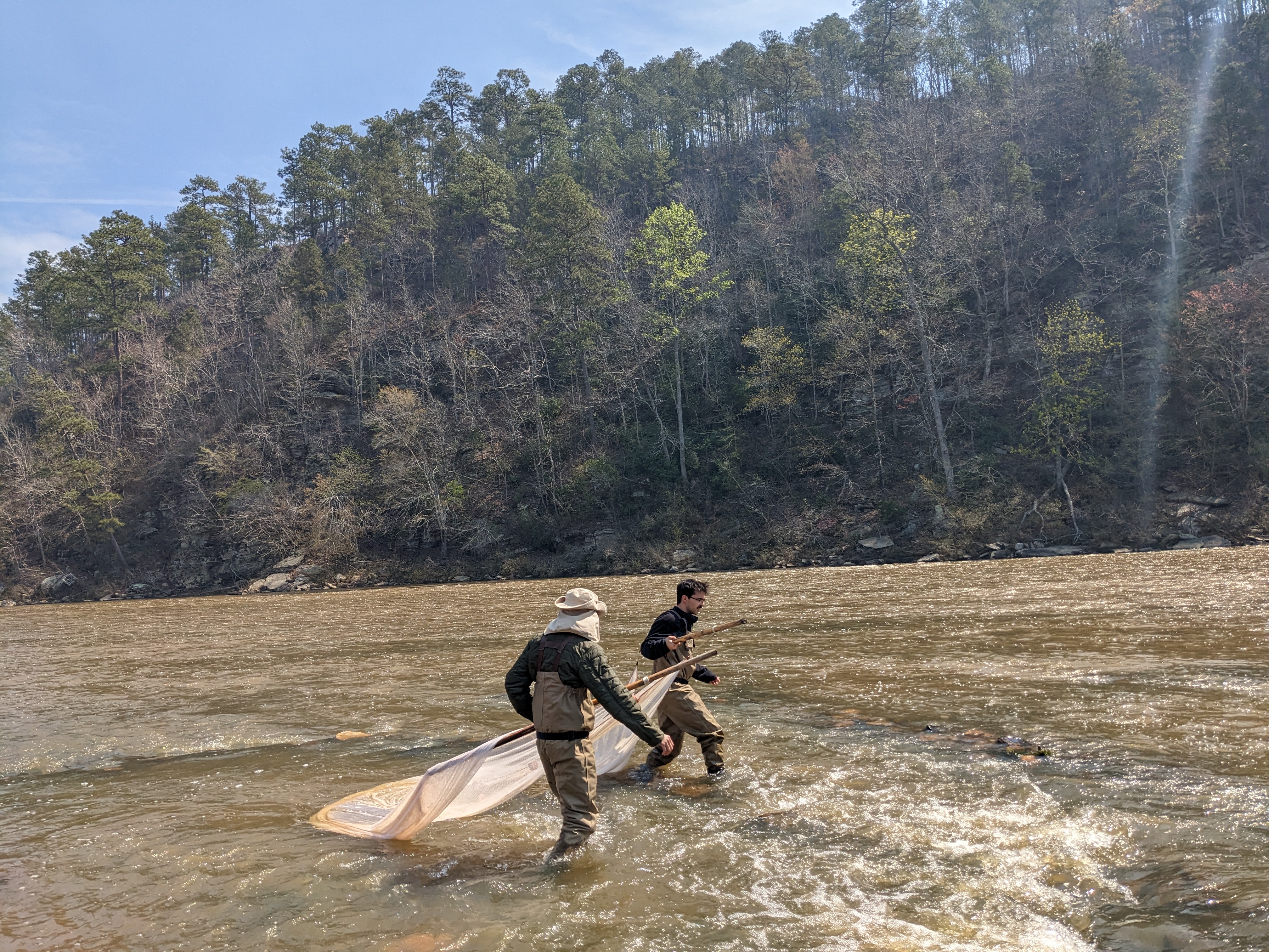 Two people dragging a river with trees in the background