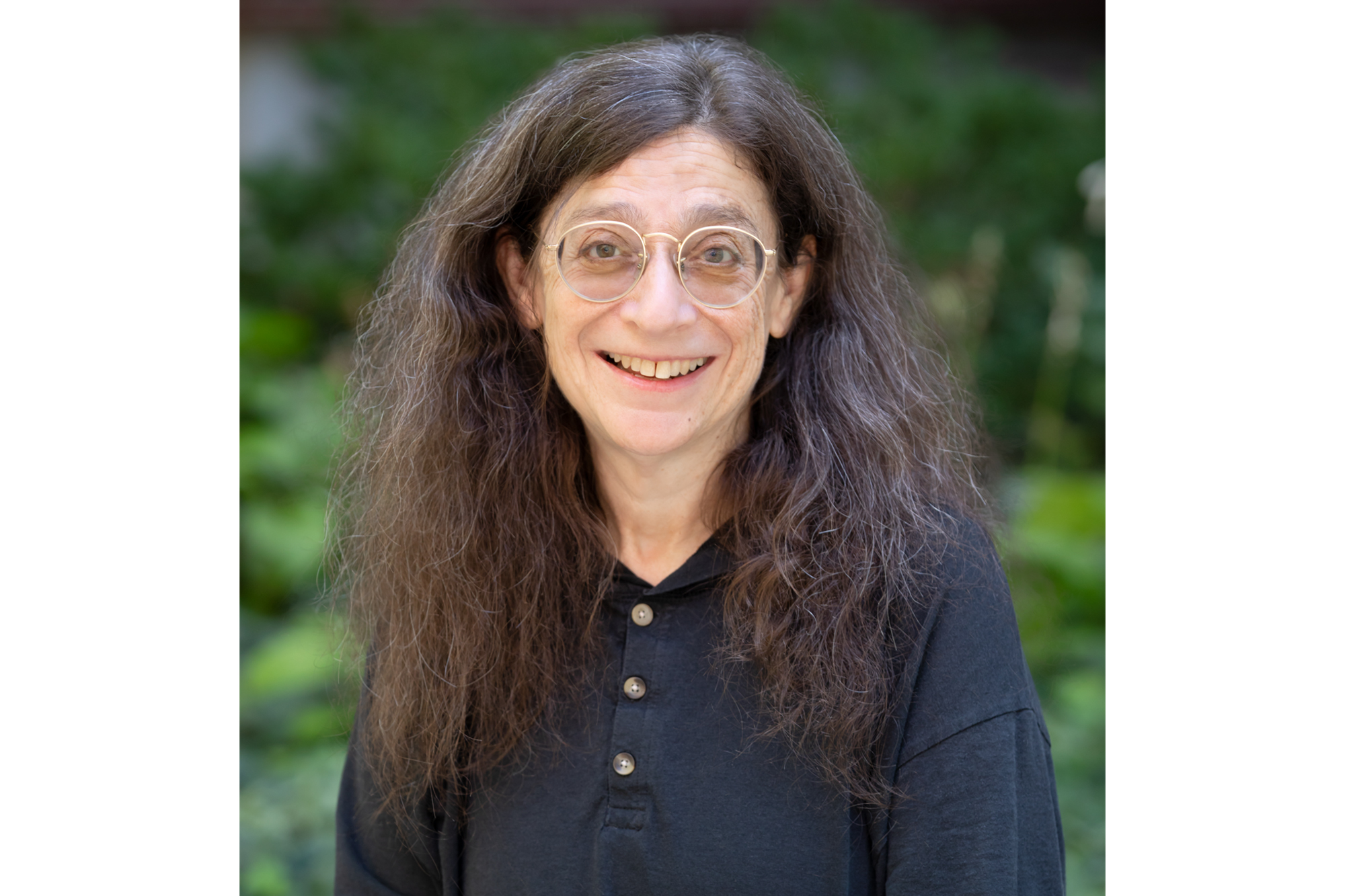 A smiling woman in a blue buttoned shirt standing outside