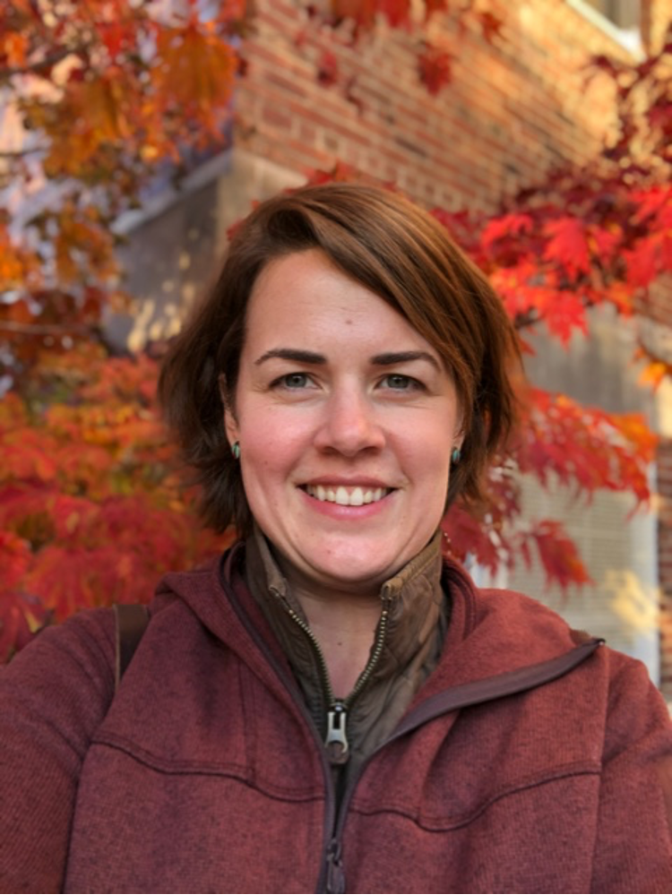 Allison O'Dwyer, Program Director, standing in front of a red leaf and brick wall background, smiling at the camera. 