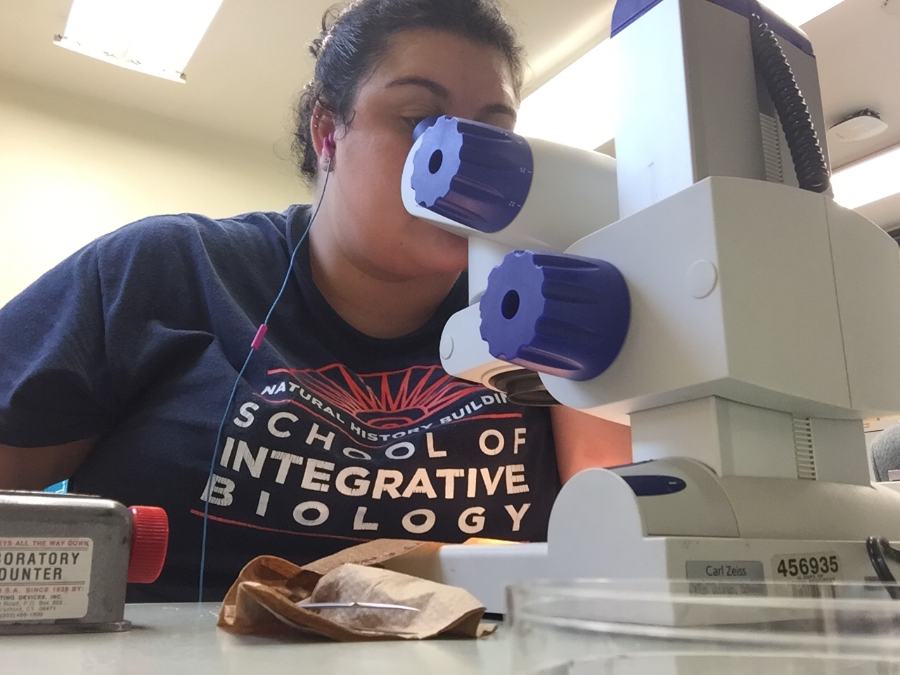 a woman looking into a microscope wearing an SIB shirt