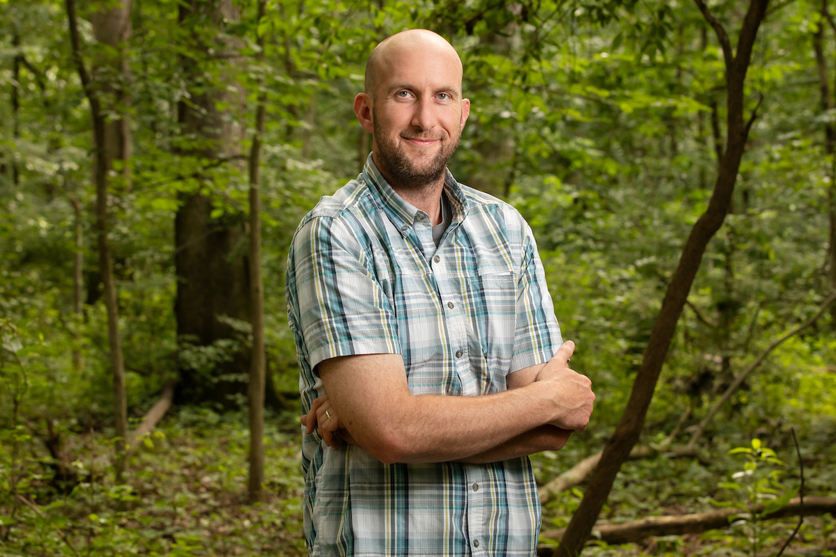 A man standing with his arms crossed in the woods