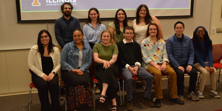 A group of students sitting and standing for a photo in front of a projector screen