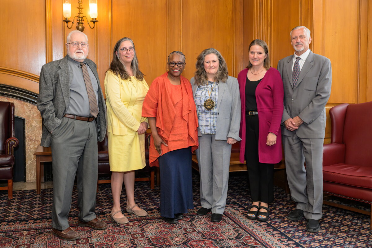 A group of people standing and smiling for a photo with a wooden wall and fireplace in the background