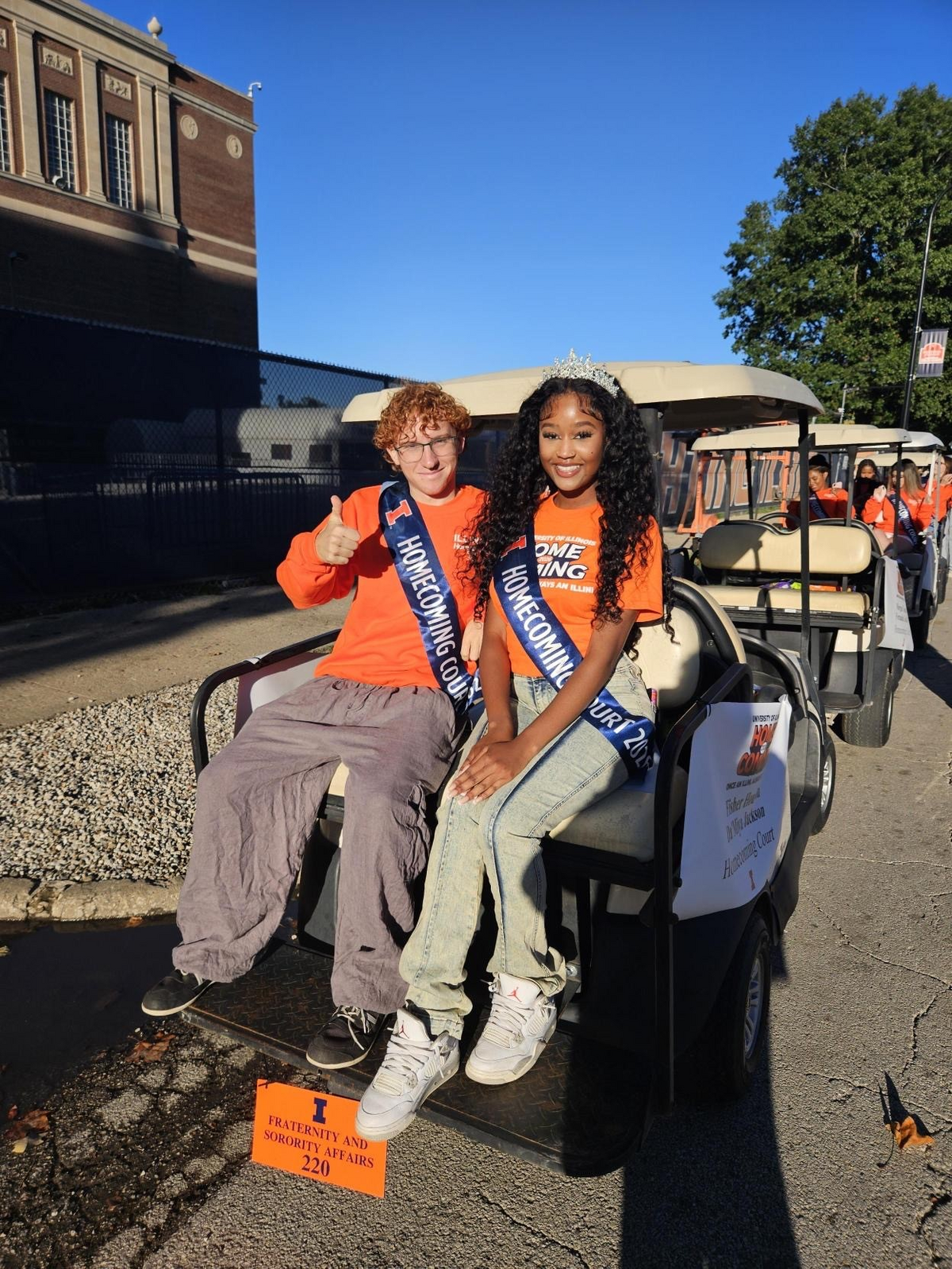 A man and a woman in orange riding the back of a cart.