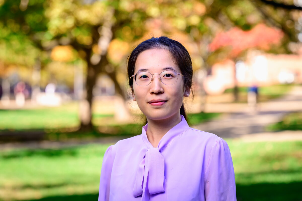 A woman in a purple shirt and glasses standing outside