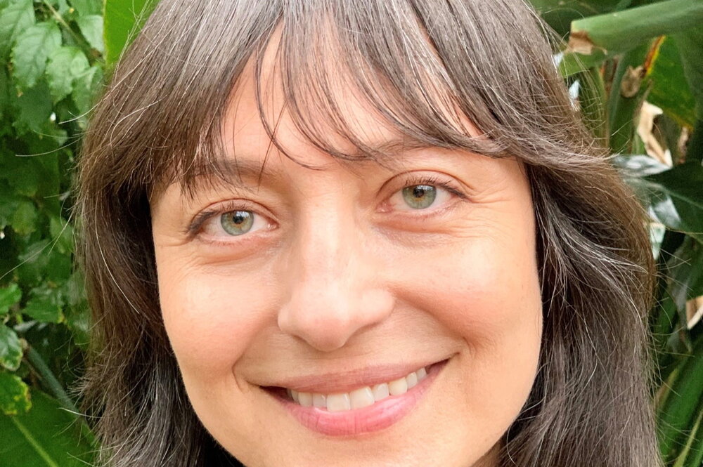A smiling woman with brown hair in front a several plants