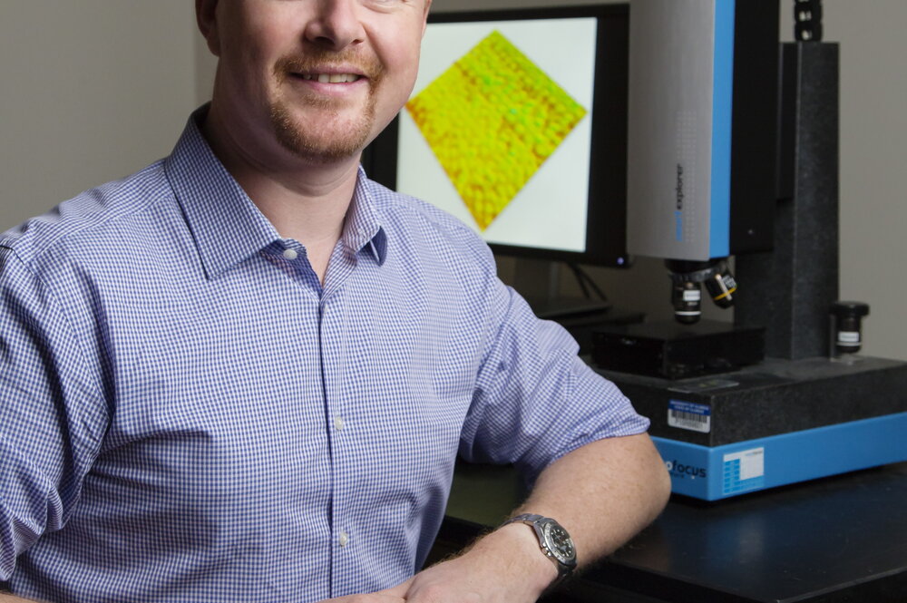 A photo of a man in a purple button up sitting next to a computer
