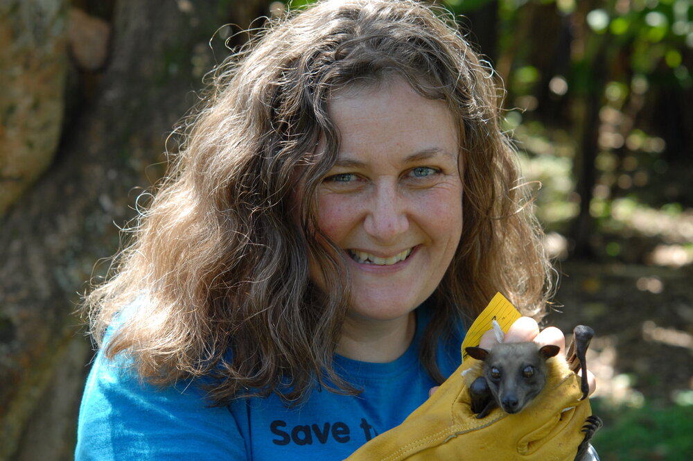 A woman in a blue shirt and yellow gloves holding a bat