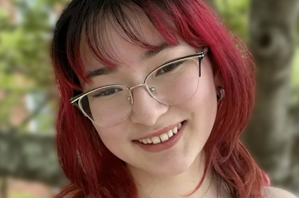 A smiling person with red hair and glasses outside