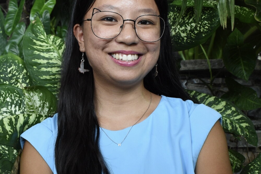 A smiling woman in a blue shirt with plants behind her