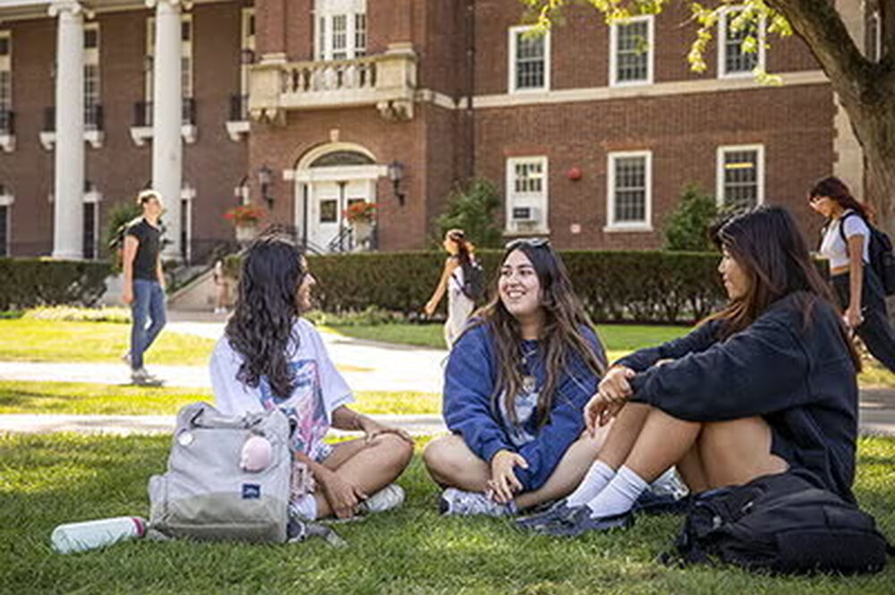 three female students sitting cross-legged on grass and talking