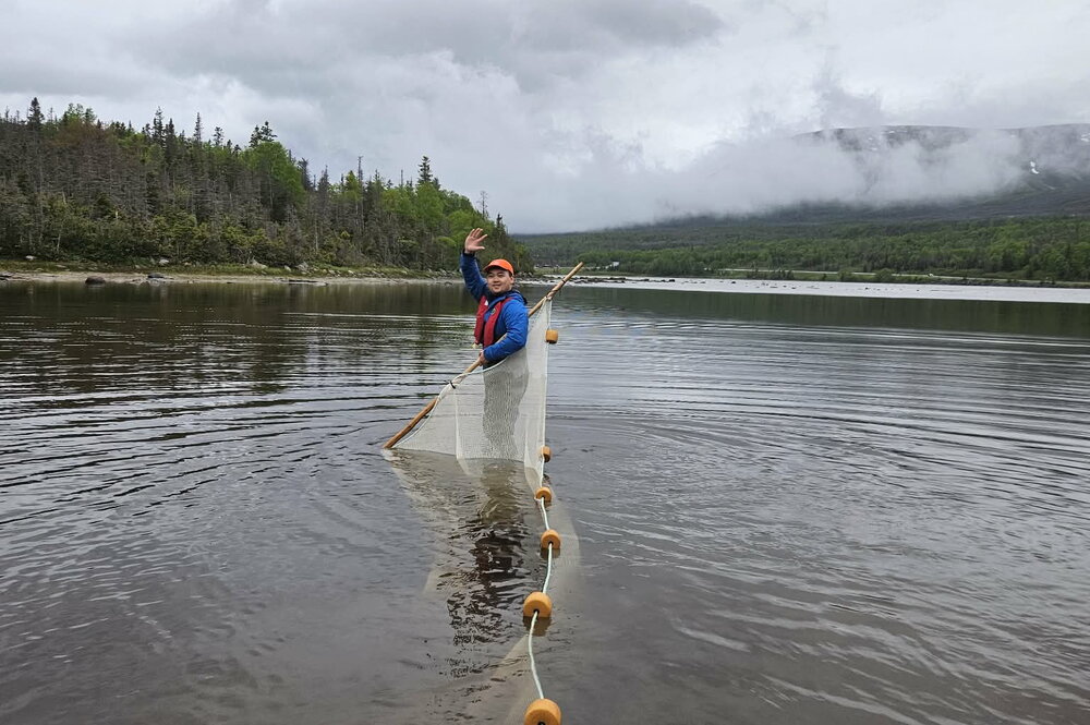 A man waving while holding a net and a rope of buoys out in water 