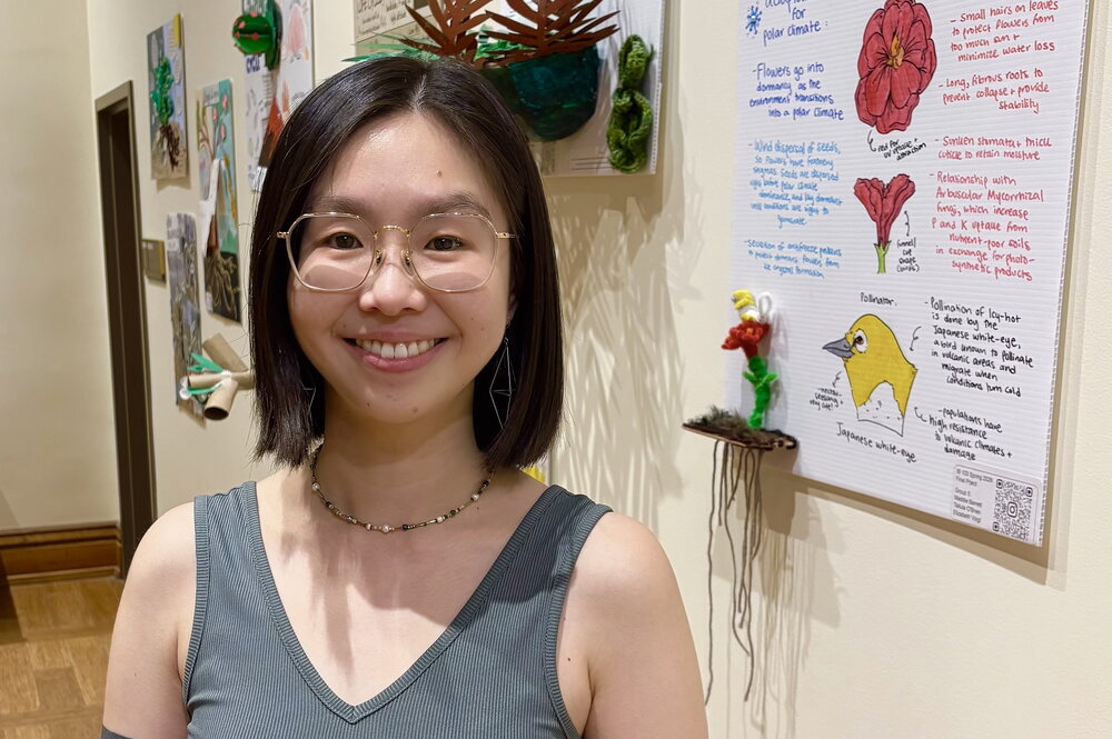 A smiling woman in a tank top standing next to posters hanging on a wall