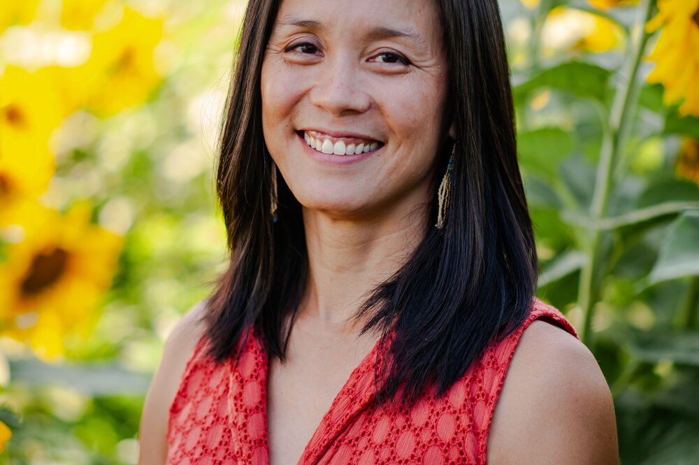 a woman smiling in a red shirt with sunflowers behind her
