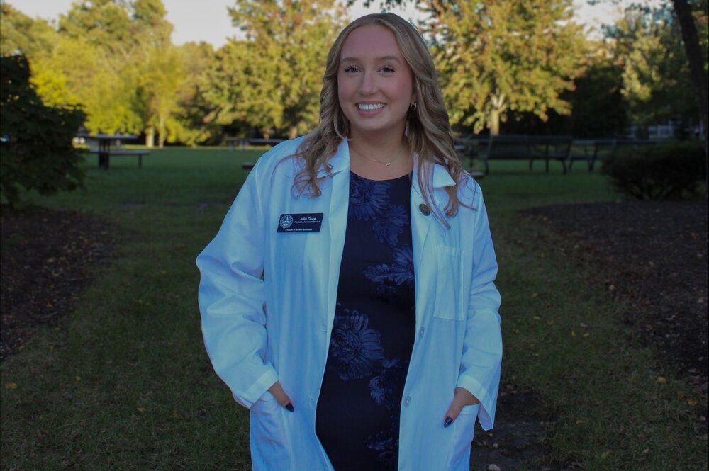 A smiling woman outside in a white lab coat