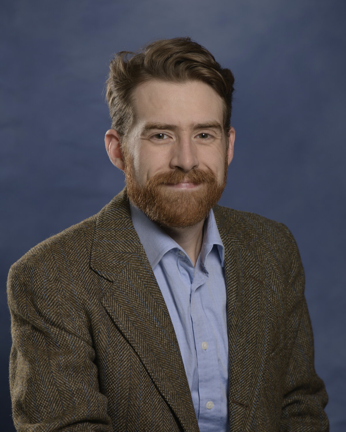 A man smiling in a sports jacket and blue button up shirt