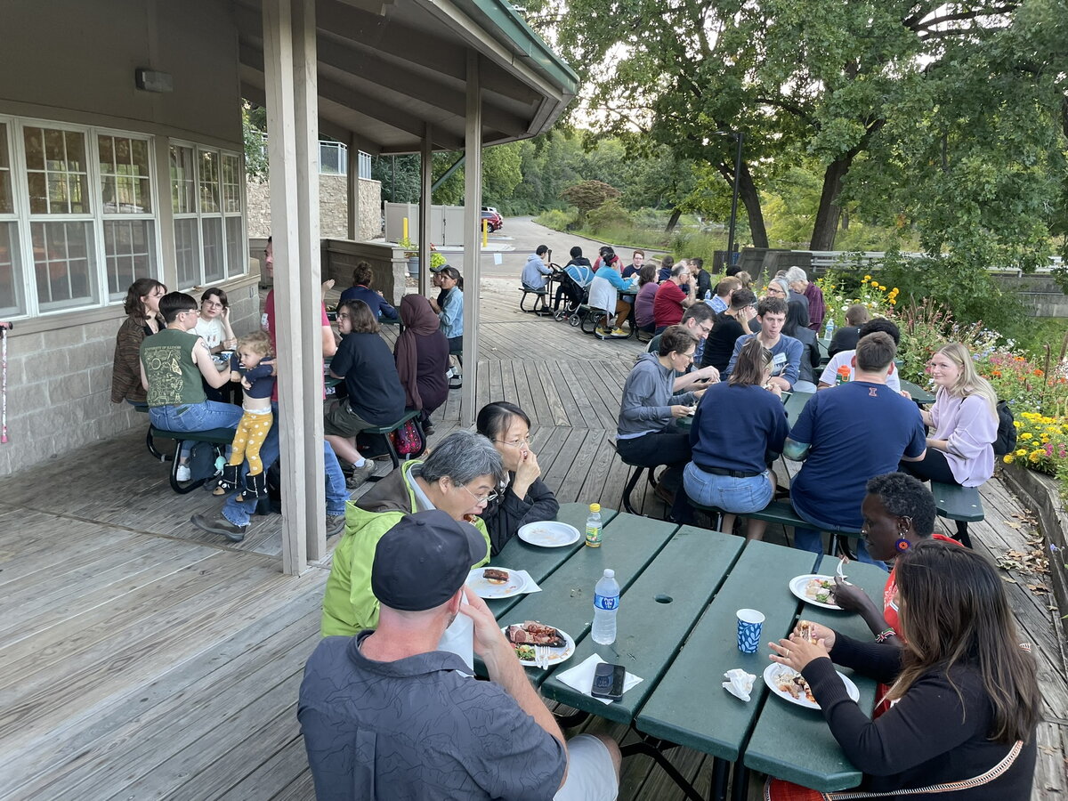 People sitting outside at picnic tables enjoying a potluck
