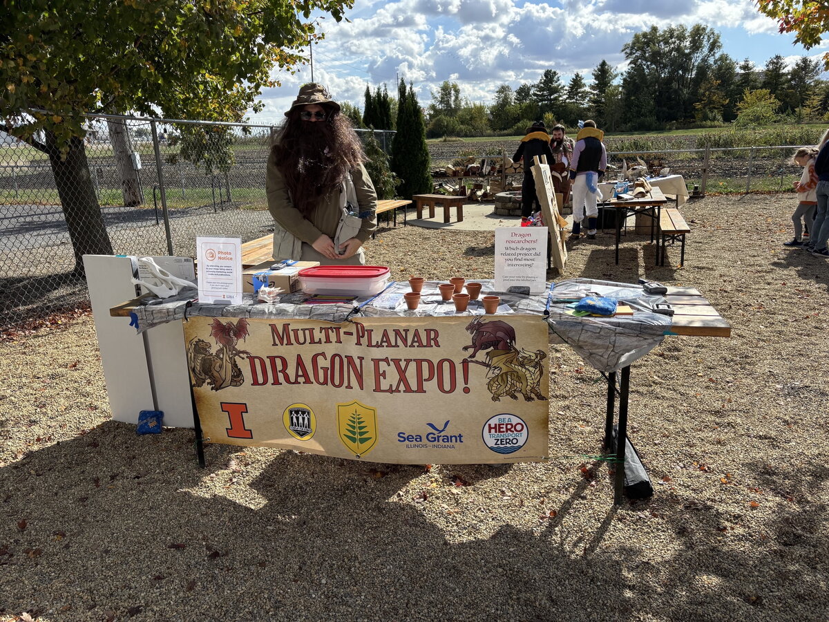 a photo of a man in a fake beard standing behind a table with a banner