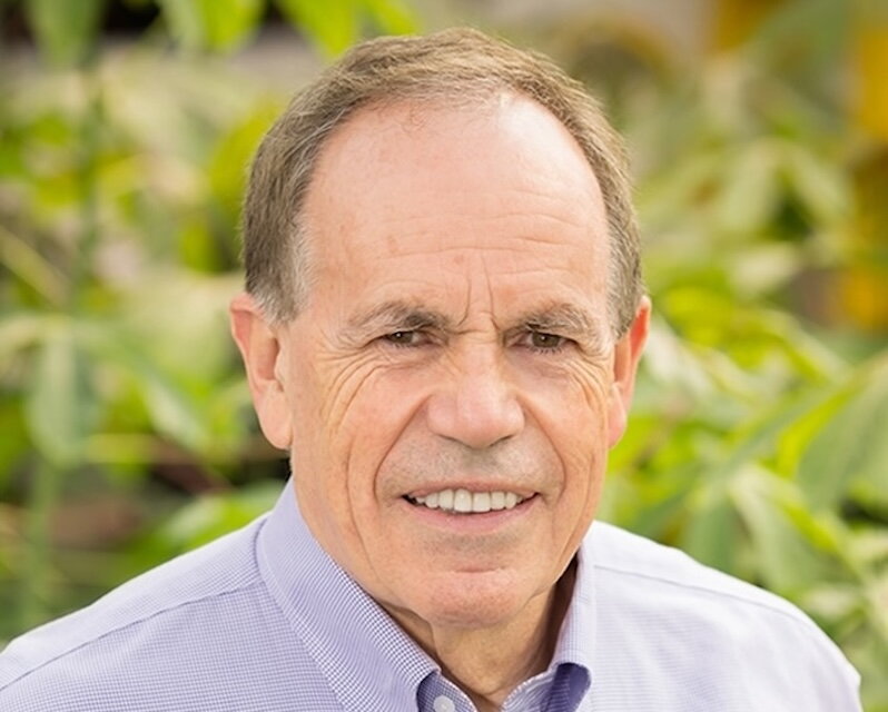 a man in a purple button up shirt with plants in the background