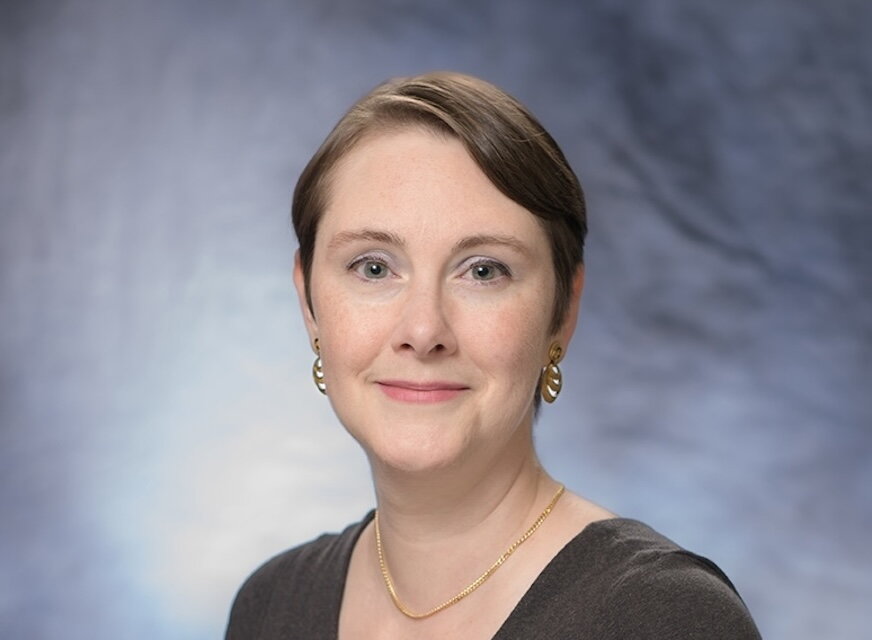 a woman in a dark gray v-neck in front of a blue background