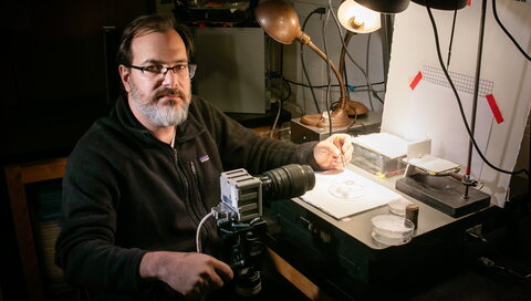 man sitting at desk with camera and pencil