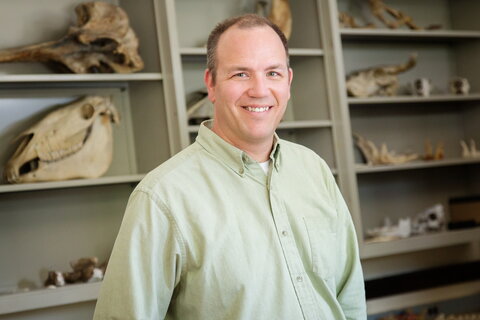 smiling man in front of shelves with animal skulls