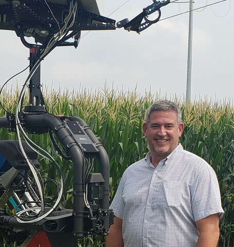 A photo of a man with a machine standing next to a corn field