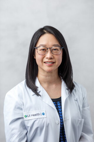 A woman with long black hair wearing glasses and a lab coat