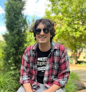 A photo of Matt Doremus sitting in front of trees in a park