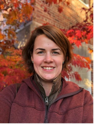 A photo of a person in a maroon coat in front of a leafy foilage