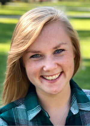A photo of a person in a turquoise plaid shirt standing in front of a green field