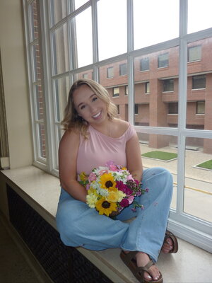 Julia sitting in a window holding pink white and yellow flowers