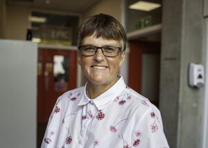 A photo of a woman in glasses in a white and red polo with a lab in the background