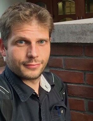 A man in a blue polo standing next to a brick wall