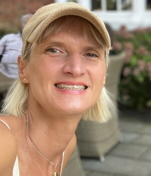 A photo of a woman in a hat with a brick wall and window in the background