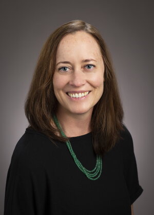 a woman with brown hair in a black shirt and a green necklace