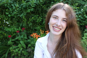 A smiling woman in white in front of leaves and flowers