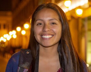 A smiling woman with long hair standing in front of a well lit street at night