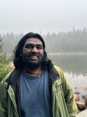 A smiling man in a jacket standing out by a river