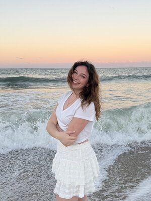 A smiling woman in a white dress standing next to the ocean