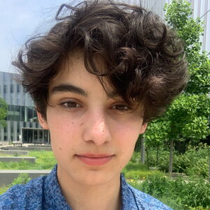 A person with curly brown hair in a blue shirt standing outside