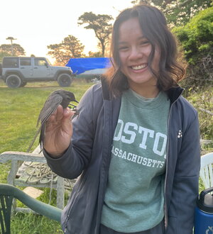 A smiling woman in an open zipper hoodie holding a bird outside