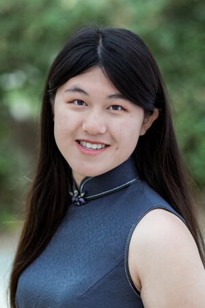 A smiling woman with long black hair standing outside